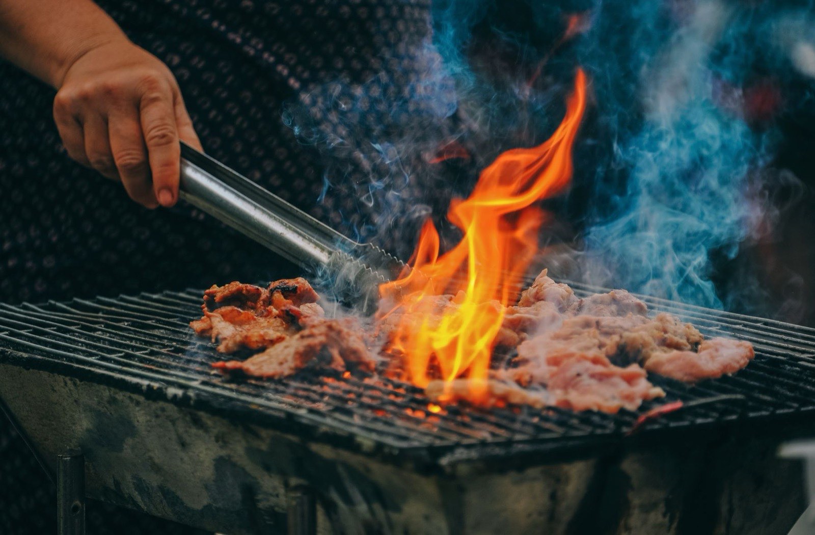 Carne asándose en la parrilla entre llamas, con unas pinzas de metal