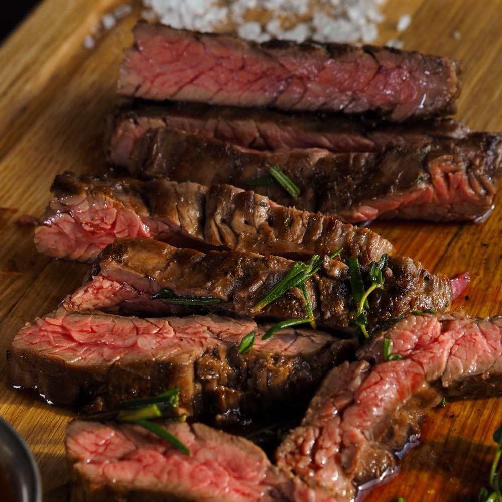 Carne a la brasa cortada en lonchas, rosada por dentro, sobre una tabla de madera
