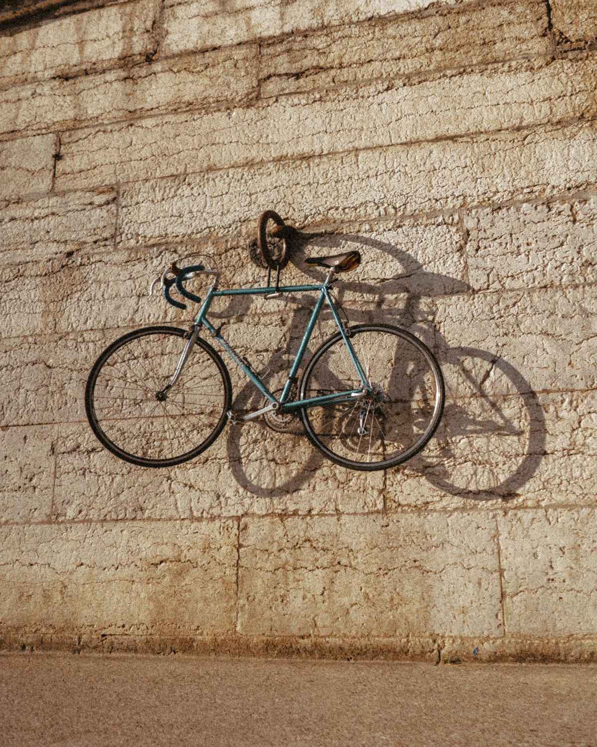 Bici de carretera clásica azul colgada en una pared de piedra al sol de la tarde